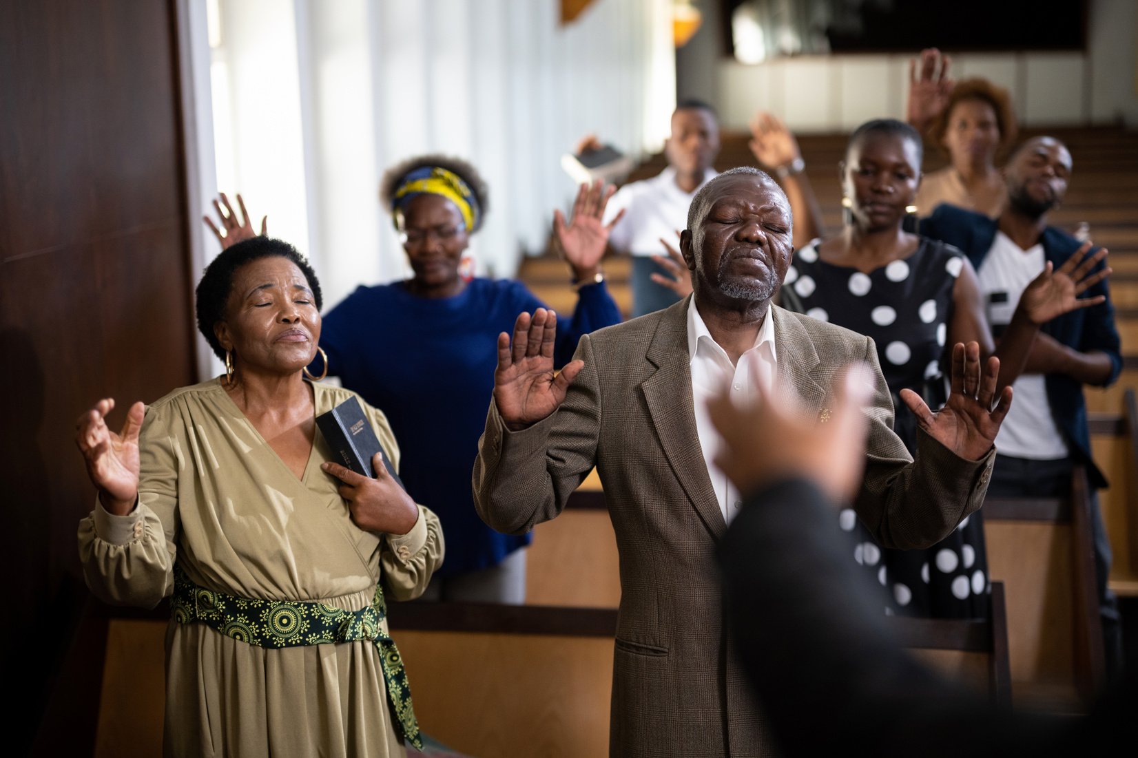 Senior couple stand praying with hands raised in church service